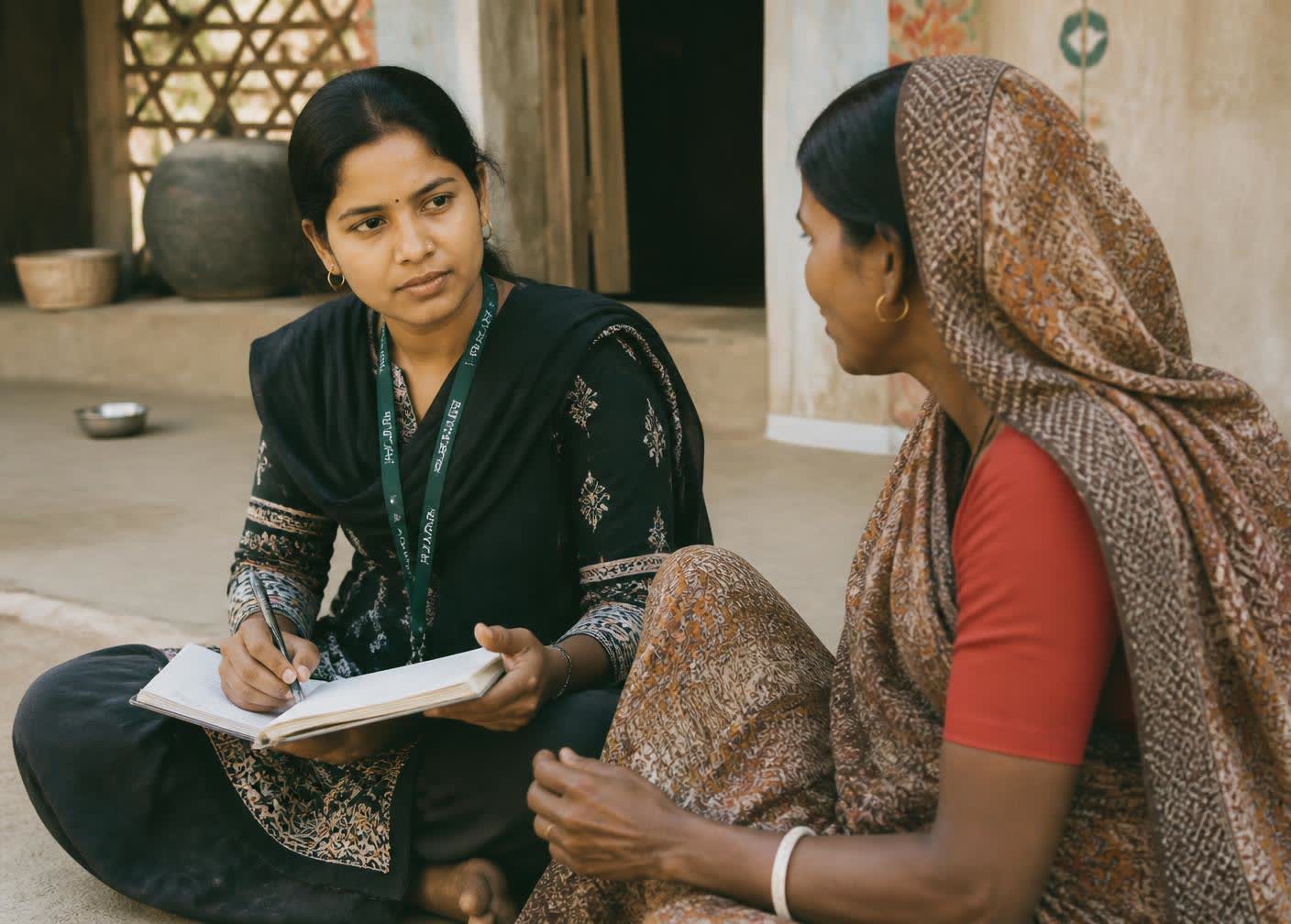 A Mehnatkash field worker sitting with a woman in her village, listening as she describes her situation